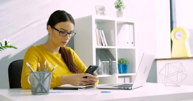 Çekici kadın gözlük, Ofis Büro iş ofiste otururken akıllı telefon kullanarak. İş kadın kapalı cep telefonu kullanarak kapatın.