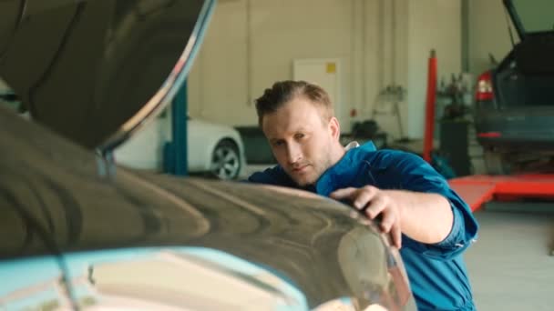 Portrait d'un jeune mécanicien automobile caucasien sérieux utilisant une clé à douille pour écrous du vissé sous le capot de la voiture. Intérieur . — Video