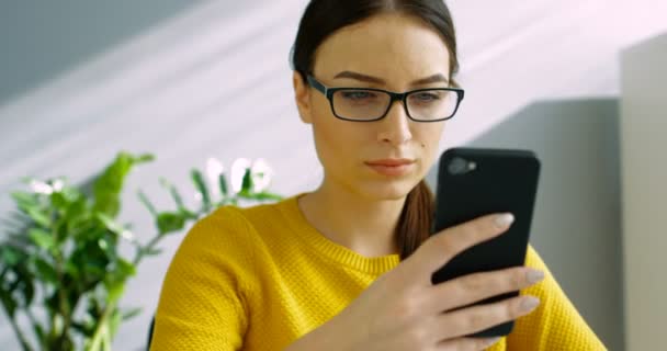Mujer atractiva en gafas usando un teléfono inteligente en la oficina. Cierre mujer de negocios utilizando el teléfono celular en el interior. Primer plano. — Vídeo de stock