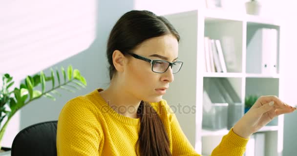 Уставшая молодая женщина снимает очки и массирует глаза. Женщина в офисе с уставшими глазами, головной болью. Закрыть — стоковое видео