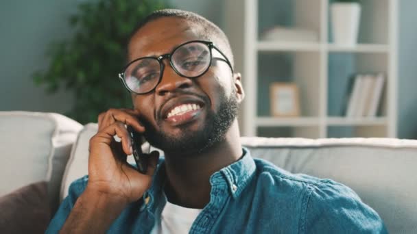 Young african man talking on the phone while sitting on the sofa at home. Close up. — Stock Video