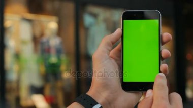 Siyah akıllı telefon ile yeşil perde vitrin arka planda tutan adam. Kaydırma, dokunarak, swiping, dokunmatik ekran yakınlaştırma. Yakın çekim. Chroma anahtar