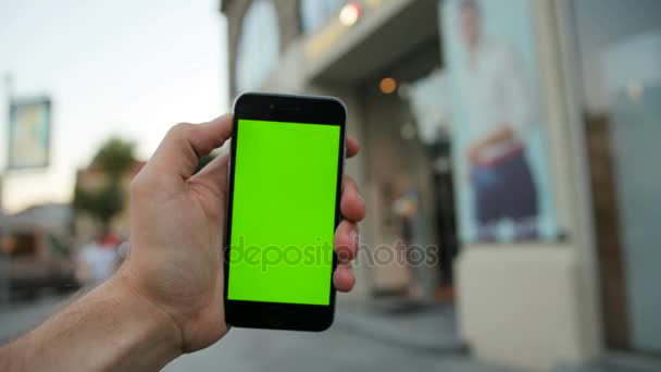 Hombre sosteniendo teléfono inteligente negro con pantalla verde en el fondo de la vitrina. Fondo de la calle City. De cerca. Clave de croma — Vídeos de Stock