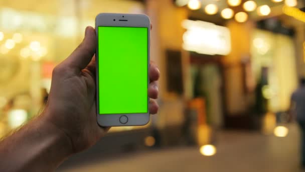 Hombre sosteniendo teléfono inteligente blanco con pantalla táctil de color verde en el fondo de la calle de la ciudad en la noche. Hermoso edificio con luces. De cerca. Clave de croma — Vídeos de Stock