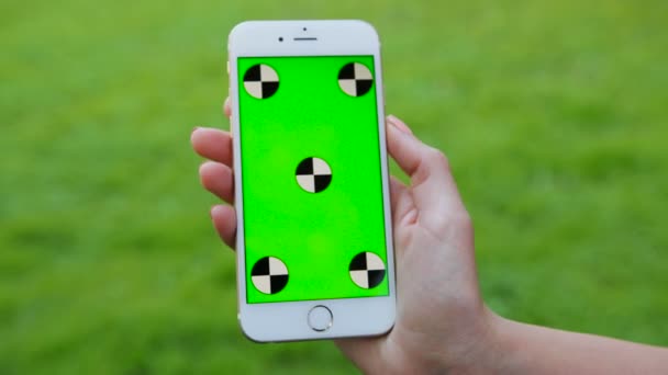 Mužské ruky držící bílý smartphone s zeleným plátnem na zelené trávě pozadí. Venku v parku. Chromatický klíč. Zblízka. Sledování pohybu — Stock video