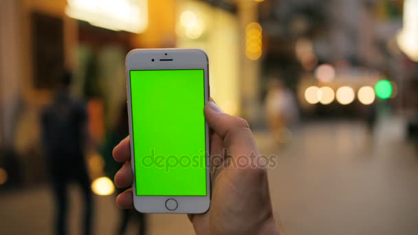 Mani maschili che tengono lo smartphone bianco verticale con schermo verde sullo sfondo della strada della città la sera, la notte. Chiudete. Chiave cromatica — Video Stock