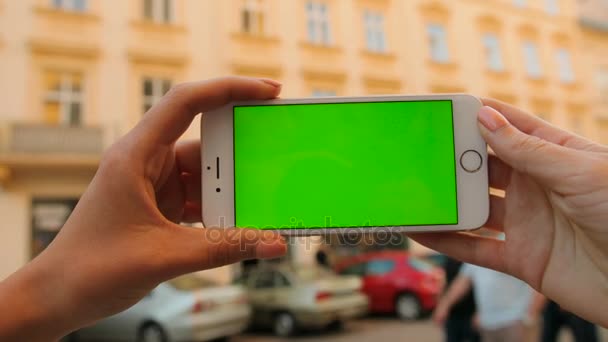 Manos de mujer sosteniendo teléfono inteligente blanco con pantalla verde al aire libre en el fondo de la calle de la ciudad. Horizontal. Clave de croma. De cerca. — Vídeos de Stock