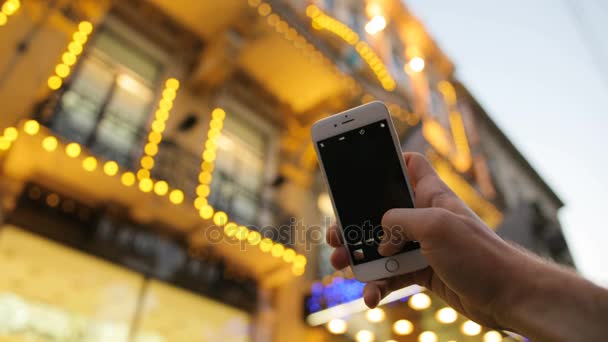 Homem fazendo fotos tiros no telefone inteligente branco ao ar livre na cidade. Boa noite, noite. A tirar fotos do edifício. Avistamento — Vídeo de Stock