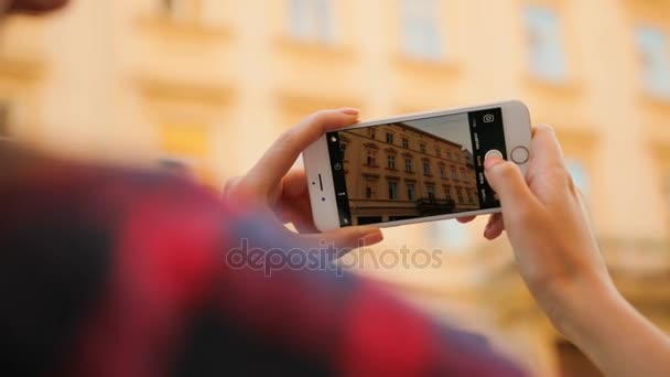 Mujer joven haciendo fotos de hermoso edificio en su teléfono inteligente blanco. Vista trasera. Avistamiento. De cerca. — Vídeo de stock