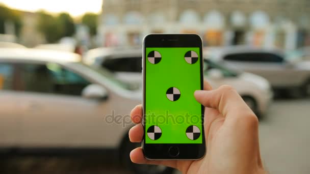 Male hands holding back smartphone with green screen on the city street background. Cars background. Man tapping, scrolling on touch screen. Close up. Chroma key. Tracking motion — Stock Video