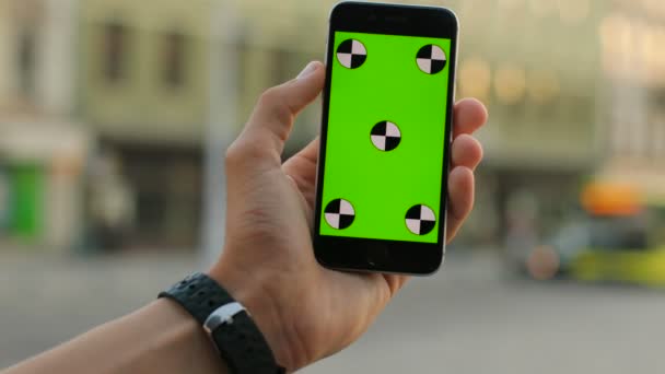 男性の手は、街の通り背景に緑色の画面で白のスマート フォンを保持しています。クローズ アップ。アウトドア。クロマ キー。モーションのトラッキング — ストック動画