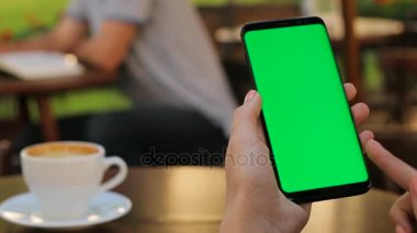 Erkek siyah smartphone ile yeşil ekran açık havada kafede otururken tutan eller. Kadın kaydırma. dokunmatik ekran yakınlaştırma. Dikey. Kahve içme kadın. Yakın çekim. Chroma anahtar