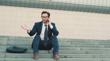 Bina ve telefonda konuşurken office center yakınındaki merdivenlerde oturan rahatsız iş adamı. Adam üzgün ve hayal kırıklığına.