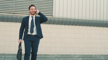 İşitme iyi haber mutlu, duygu da cep telefonda konuşurken merdivenlerden aşağı yürüme çekici iş adamı. Adam ellerini yükselterek. Açık havada şehirde ofis binası yakınındaki