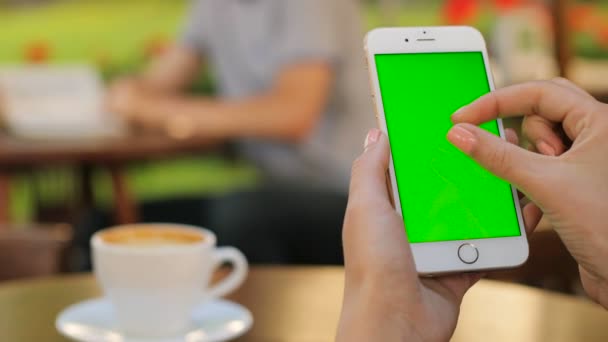 Les mains féminines tenant smartphone blanc avec écran vert tout en étant assis à l'extérieur dans le café. Femme défilant. zoom sur écran tactile. Verticale. Une femme qui boit du café. Ferme là. Clé chromatique — Video