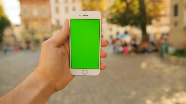 Uomo in possesso di smart phone bianco con schermo verde sullo sfondo della strada della città nella giornata di sole. Chiave cromatica. Da vicino. — Video Stock