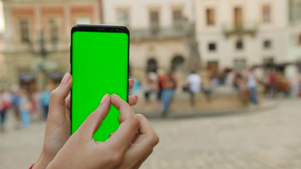 Hombre sosteniendo teléfono inteligente negro con pantalla verde en el fondo de la calle de la ciudad en el día soleado. Gran pantalla. Hombre desplazándose, acercándose.Cobblet street background. Clave de croma. De cerca. — Vídeo de stock