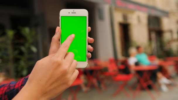 Manos femeninas sosteniendo teléfono inteligente negro con pantalla verde en el fondo de la cafetería de la calle. Mujer desplazándose, deslizando fotos, acercándose. De cerca. Clave de croma . — Vídeos de Stock