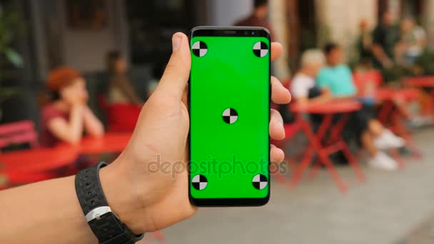 Homem segurando smartphone preto com tela verde no fundo do café de rua. Fecha. Chave Chroma. Movimento de rastreamento — Vídeo de Stock