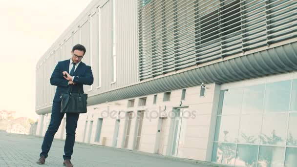 Attraktiv ung affärsman talar på mobilen, tittar på klockan och kör till ett möte nära kontorsbyggnad center. Man är sen till jobbet, möte. Slow motion. — Stockvideo