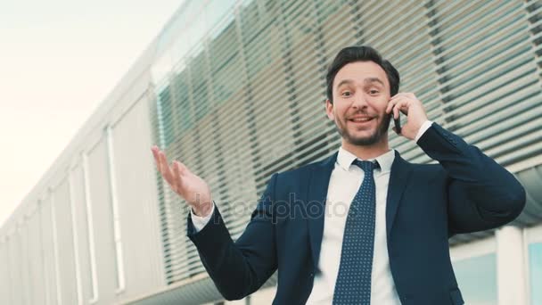 Um empresário qualquer a ter uma boa conversa no telemóvel. A ouvir boas notícias. Um homem a olhar para a câmara com emoções felizes. Tiro ao ar livre. de perto — Vídeo de Stock