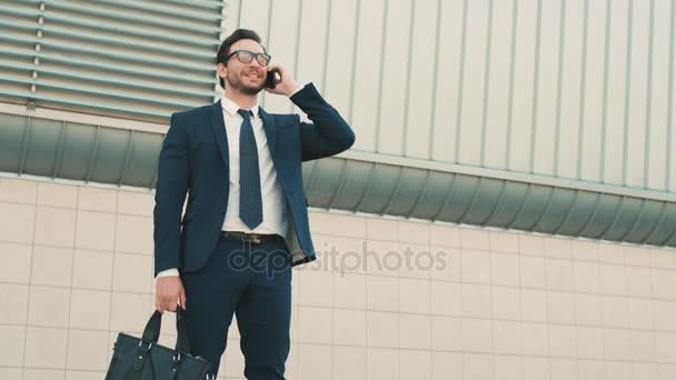 Elegante joven hombre de negocios teniendo conversación en el teléfono móvil fuera cerca de gran edificio de oficinas . — Vídeos de Stock