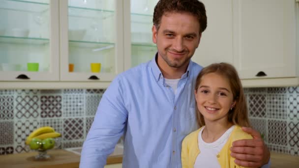 Feliz padre y su hermosa hija sonriendo y posando en cámara en la cocina . — Vídeos de Stock