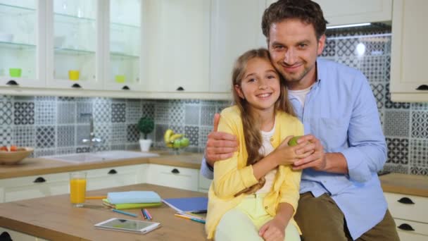 Retrato de padre feliz y su hermosa hija sonriendo y posando en cámara en la cocina . — Vídeo de stock