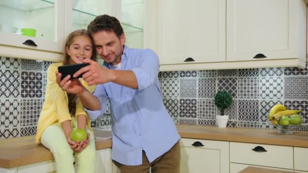 幸せな父と彼の笑顔の美しい娘とキッチンで selfie をしながらスマート フォンでカメラに possing. — ストック動画