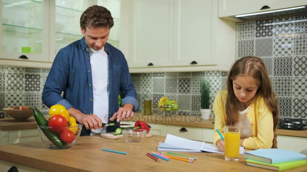 Schattig jong meisje tekening van de foto's op de keuken terwijl haar vader snijden de rode peper. — Stockvideo