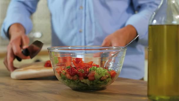 Молодой человек руки резки помидоры и перец и положить ингредиенты в стеклянную миску к салату . — стоковое видео