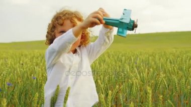 Yakışıklı ufaklikla yeşil buğday alanında mavi ahşap uçak oyuncak ile oynarken bukleler. Yakın çekim. Portre vurdu