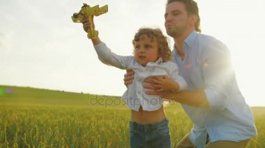 Onun güneşi gökyüzüne ahşap uçak ile yükselterek baba. Adam ve küçük çocuk yeşil buğday alanında oynuyor. Yakın çekim