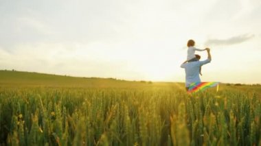 Omuzlarında yeşil buğday alanı oğlu ile çalışan baba. Uçurtma uçan ile oynayan çocuk. Arka görüş. Sunset bulvarında
