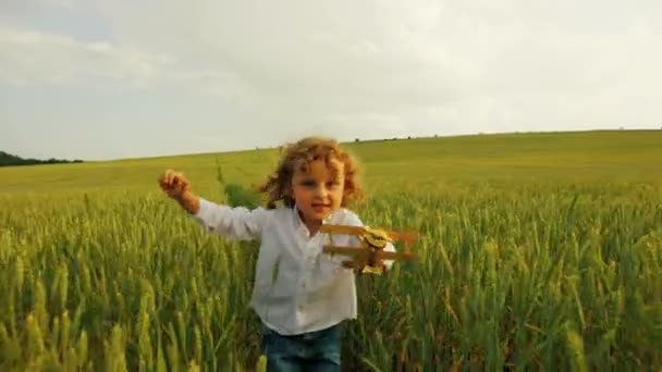 Beau petit garçon courant vers dans le champ vert avec avion jouet jaune. Gros plan — Video