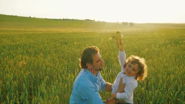 Szczęśliwa rodzina, ojciec i syn, grając razem z drewniany samolot zabawka zielony pole w słoneczny dzień. z bliska — Wideo stockowe