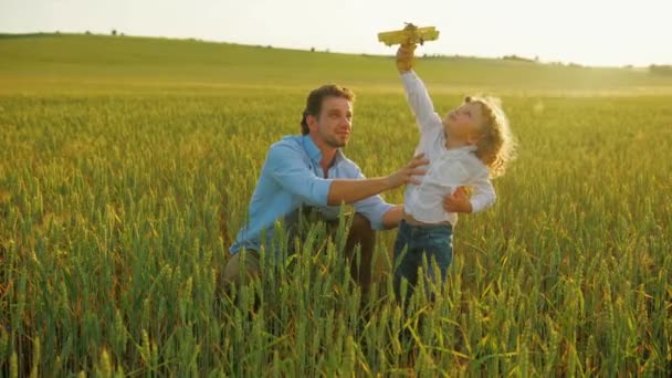 Gelukkig gezin, vader en zoon spelen samen met houten vliegtuig speelgoed in groene veld. Close-up — Stockvideo