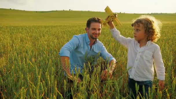 Little boy playing with toy airplane with his father on green wheat field. Close up — Stock Video