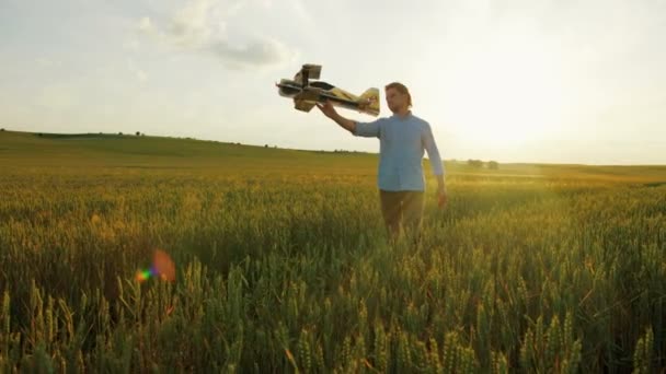 Junger kaukasischer Mann beim Spielen mit einem großen Flugzeug im grünen Weizenfeld bei Sonnenuntergang. Nahaufnahme — Stockvideo