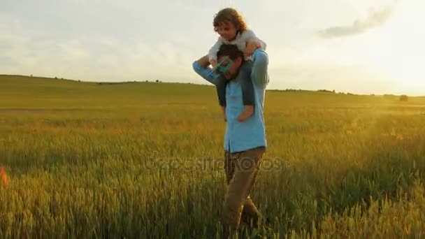 Feliz padre con hijo corriendo en el campo de trigo verde. Joven padre sosteniendo a su hijo sobre los hombros. De cerca. — Vídeos de Stock