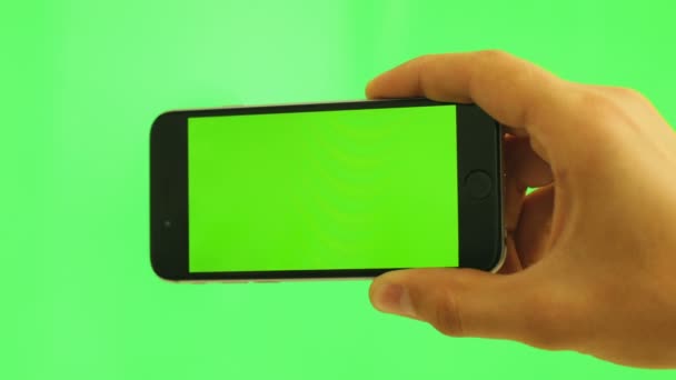 Cierre el teléfono celular horizontal con pantalla verde. Hombre sosteniendo teléfono inteligente negro con pantalla verde sobre fondo verde. Clave de croma — Vídeos de Stock