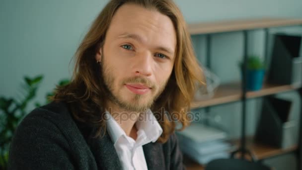 Nahaufnahme Porträt eines Geschäftsmannes mit langen Haaren, der freundlich in die Kamera blickt. Lächelnder junger Mann im Büro. — Stockvideo