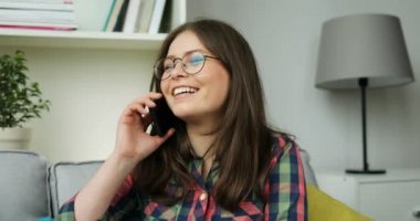 Güzel genç kız oturma odasında kanepede otururken cep telefonuyla konuşuyor. Gülümseyen kız arkadaşlarınızla telefonda konuşurken.