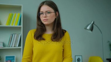 Genç kız evde oturma odasında dururken ciddi bir yüz ile kameraya bakarak portresi.