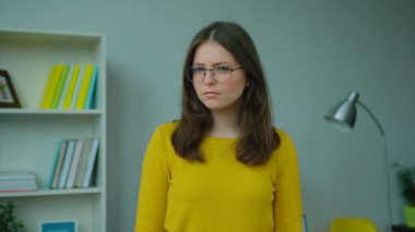 Kameraya bakarak ve evde oturma odasında dururken gülümseyen genç kız portresi.