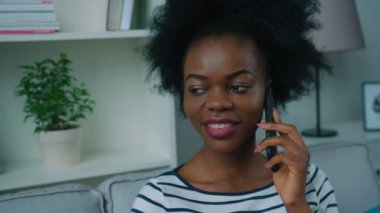 Afrikalı-Amerikalı kadın oturma odasında kanepede cep telefonuyla konuşuyor. Yakın çekim