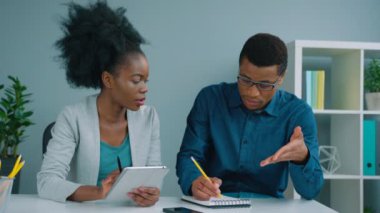 Takım birlikte ofiste çalışan iki Afro-Amerikan iş adamları. Afrika kökenli Amerikalı işadamı ve konuşurken, tablet cihaz kullanarak, mali çizelgeleri kontrol işkadını.