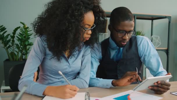 Una squadra di due uomini d'affari afroamericani che lavorano insieme in ufficio. Uomo d'affari e donna d'affari afroamericani che parlano, usando tablet, controllando i grafici finanziari . — Video Stock