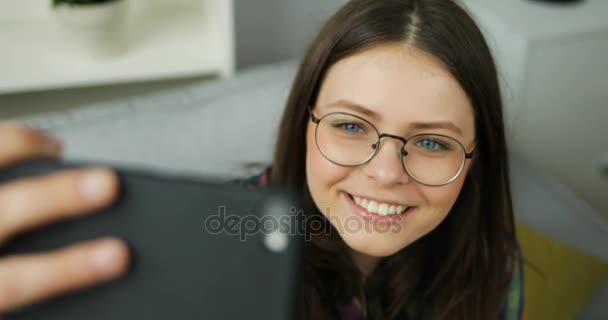 Menina adolescente bonita fazendo selfies enquanto sentado no sofá na sala de estar. Menina sorrindo para a câmera e fazendo fotos. Fechar — Vídeo de Stock