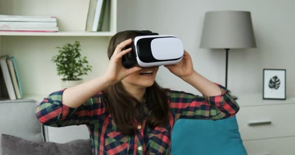 Ragazza adolescente che guarda video con auricolare vr. Giovane ragazza seduta sul divano e utilizzando occhiali di realtà virtuale a casa. Ragazza chiedendo — Video Stock